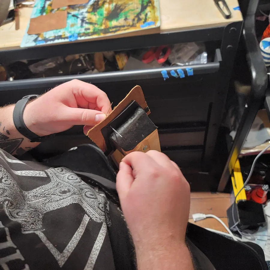 The maker saddle-stitching a piece by hand at the workbench
